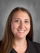 Smiling woman with long brown hair and a black shirt, against a gray background.
