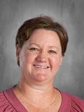 Smiling person with short hair wearing a pink top, set against a gray background.