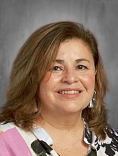 Smiling woman with shoulder-length hair, wearing a floral-patterned top against a gray background.