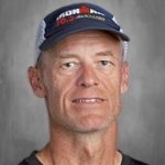 Un hombre con una camiseta oscura y una gorra con el logotipo de «Ironman 70.3», sobre un fondo gris.