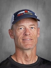 Man wearing a dark shirt and a cap with "Ironman 70.3" logo, against a gray background.