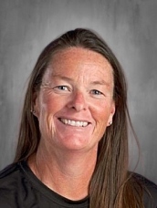 Smiling person with long brown hair, wearing a black shirt, against a gray background.