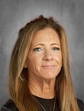 Woman with long brown hair smiling softly against a gray background.
