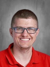 Smiling person wearing glasses and a red polo shirt against a gray background.
