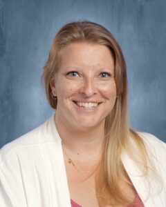 Smiling woman with long blonde hair, wearing a white cardigan over a pink top, against a blue background.