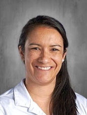 Smiling woman with long dark hair wearing a white shirt, set against a gray background.