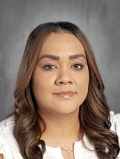 Headshot of a woman with long, wavy hair, wearing a white top, looking directly at the camera with a neutral expression.