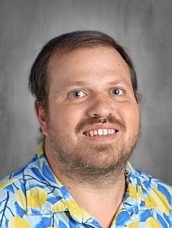 Smiling man with short hair wearing a colorful Hawaiian shirt against a plain background.
