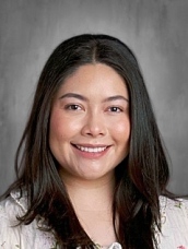Smiling woman with long dark hair in a light-colored top against a gray background.