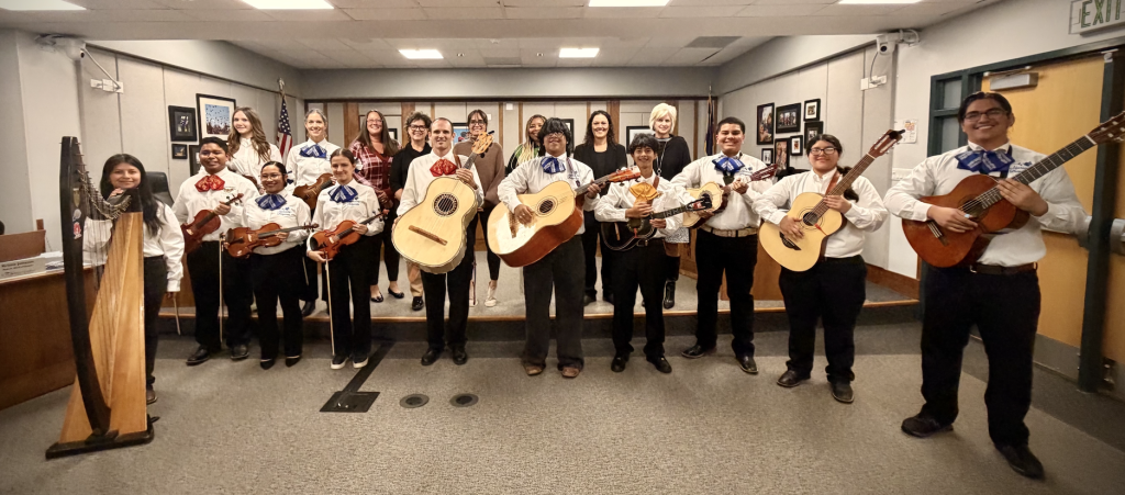 A group of students in mariachi attire holding instruments, with faculty members standing behind them.